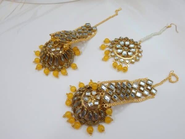 A Kundan maang tikka and matching earrings set with large fan-shaped pendants and yellow beaded drops.