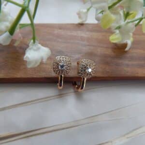 A pair of small, gold-toned huggie hoop earrings with a studded circular dome shape