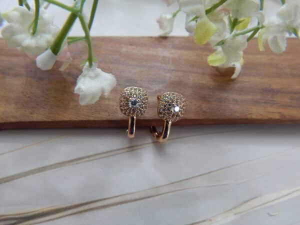 A pair of small, gold-toned huggie hoop earrings with a studded circular dome shape