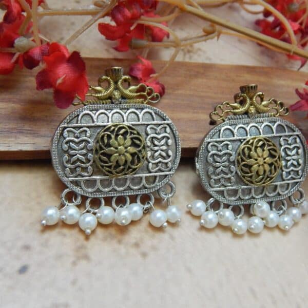 A pair of dual-tone oxidized silver and antique gold oval earrings with filigree work and white pearl dangles.