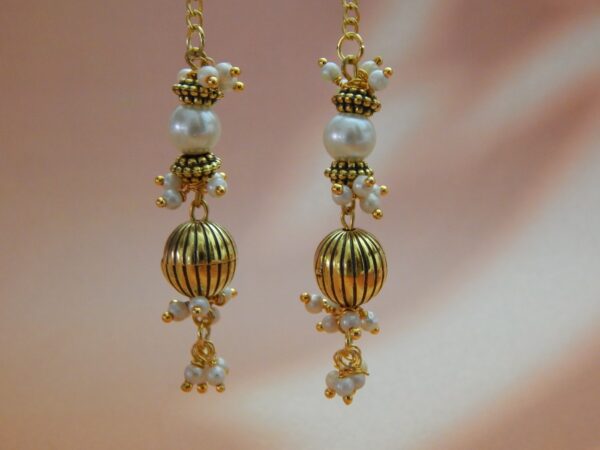A pair of long, gold-toned dangler earrings with pearl beads and a ribbed oval bead, designed in a traditional style.