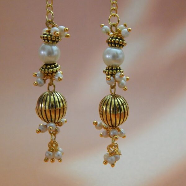 A pair of long, gold-toned dangler earrings with pearl beads and a ribbed oval bead, designed in a traditional style.
