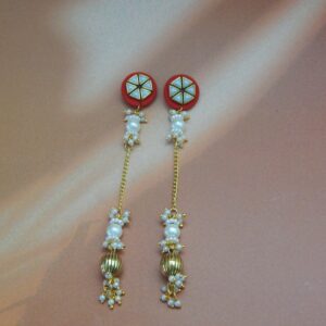A pair of long, traditional red and gold-toned earrings with a geometric stud, hanging pearl drops, and a ribbed gold bead.