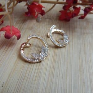 A pair of small, gold-toned open hoop earrings with a studded leaf or floral design at the base