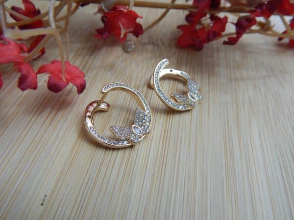 A pair of small, gold-toned open hoop earrings with a studded leaf or floral design at the base