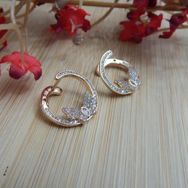 A pair of small, gold-toned open hoop earrings with a studded leaf or floral design at the base