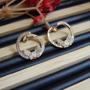 A pair of small, gold-toned open hoop earrings with a studded leaf or floral design at the base