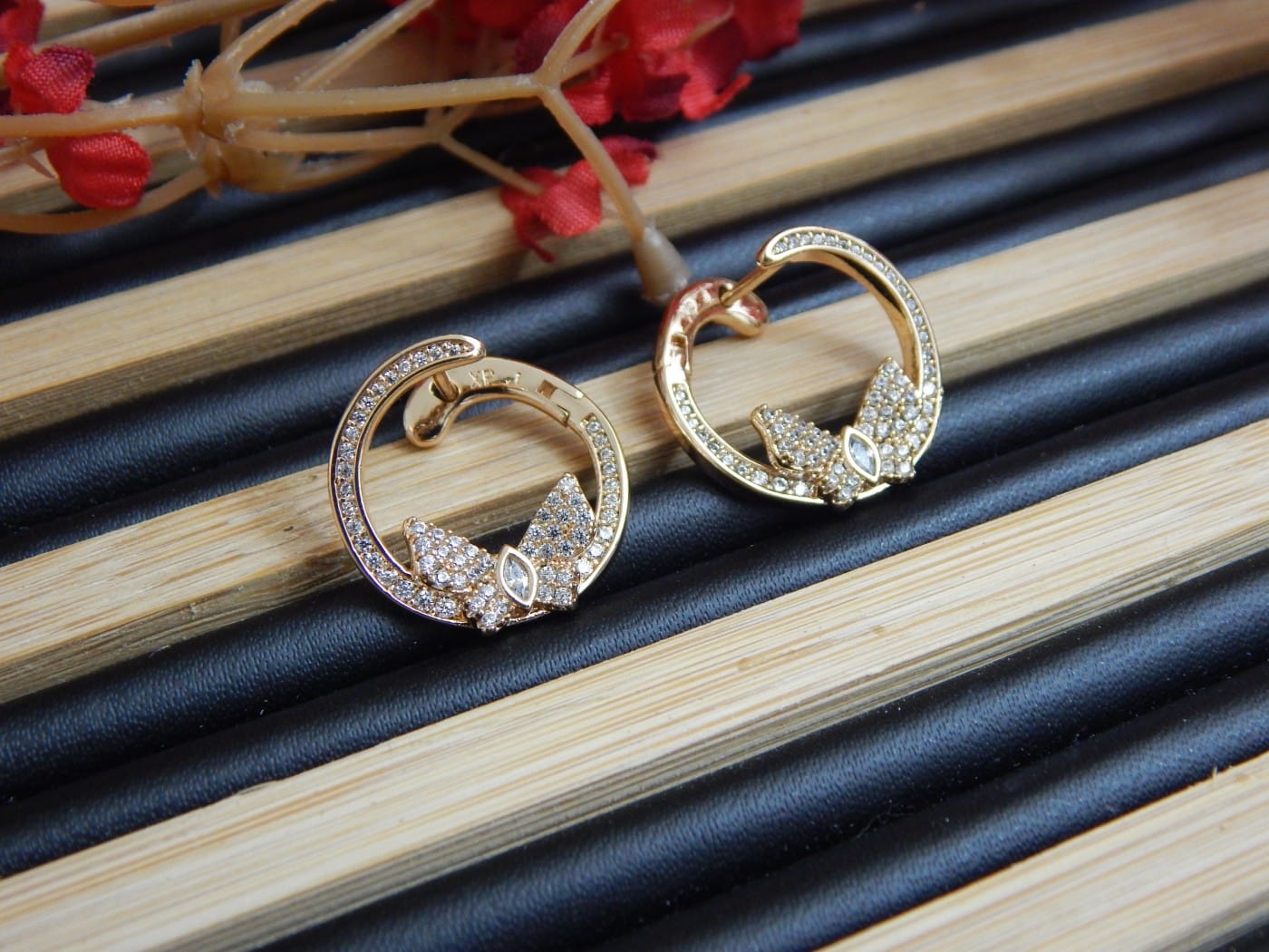 A pair of small, gold-toned open hoop earrings with a studded leaf or floral design at the base