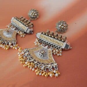 A pair of oxidised and gold-toned fusion jhumka earrings with a half-moon design and pearl drops, on a solid background