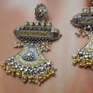 A pair of oxidised and gold-toned fusion jhumka earrings with a half-moon design and pearl drops, on a solid background