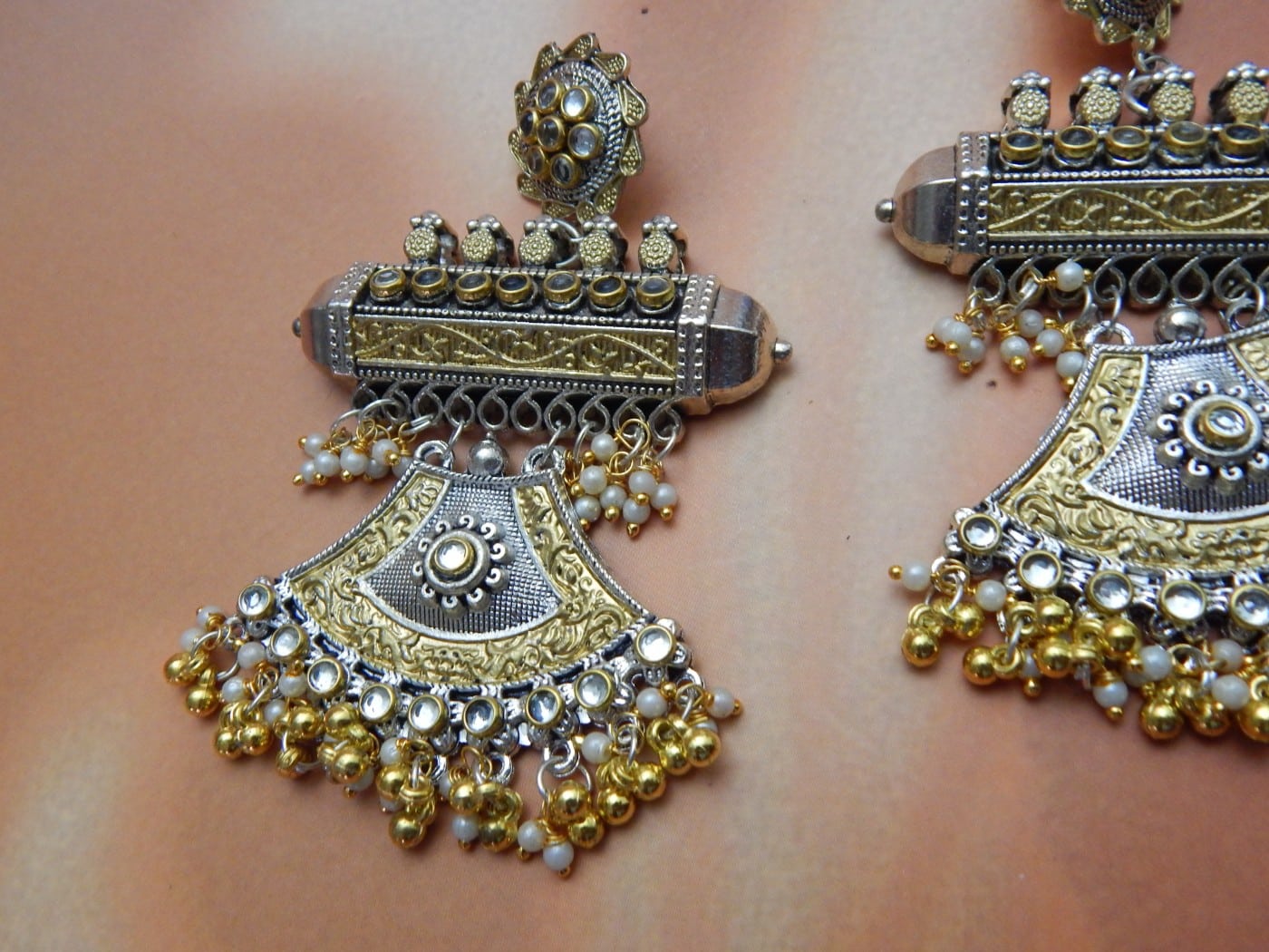 A pair of oxidised and gold-toned fusion jhumka earrings with a half-moon design and pearl drops, on a solid background