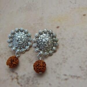 A pair of oxidised silver-toned earrings with a Ganesha motif stud and a single rudraksha bead hanging below