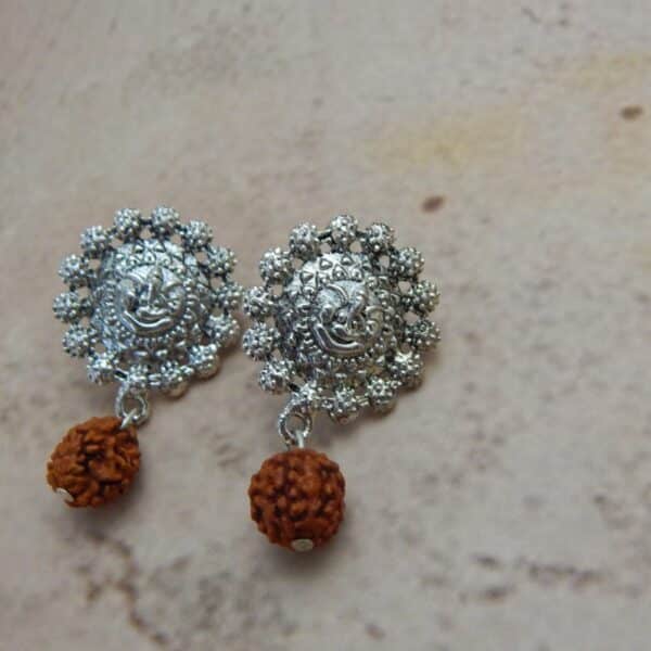 A pair of oxidised silver-toned earrings with a Ganesha motif stud and a single rudraksha bead hanging below