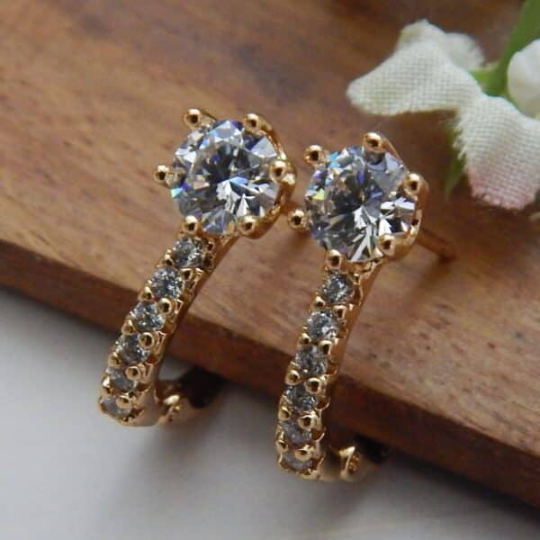 A pair of small, gold-toned earrings with a large central clear stone and a small studded hoop at the base