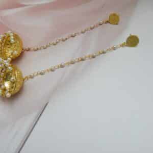 Very long gold jhumka earrings hanging from a pearl bead chain connected to a small gold disc stud.