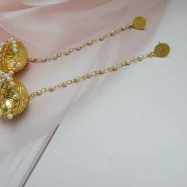 Very long gold jhumka earrings hanging from a pearl bead chain connected to a small gold disc stud.