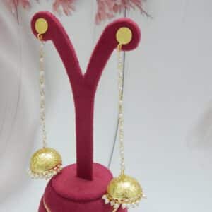 Very long gold jhumka earrings hanging from a pearl bead chain connected to a small gold disc stud.