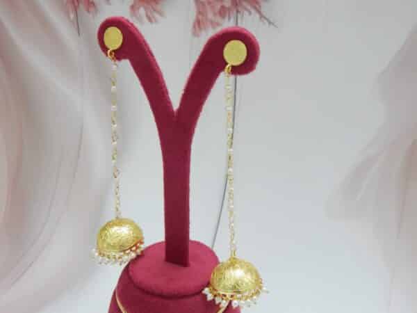 Very long gold jhumka earrings hanging from a pearl bead chain connected to a small gold disc stud.