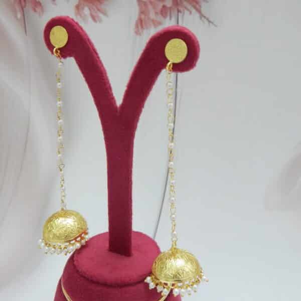 Very long gold jhumka earrings hanging from a pearl bead chain connected to a small gold disc stud.