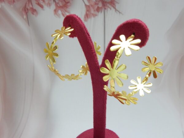 Large, bright gold-tone hoop earrings made entirely of linked daisy flower shapes.