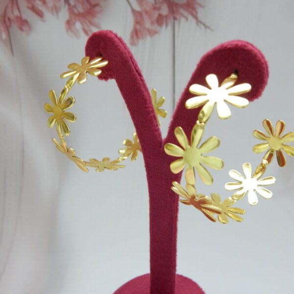 Large, bright gold-tone hoop earrings made entirely of linked daisy flower shapes.