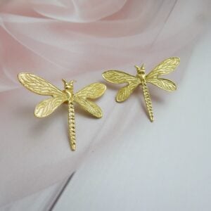 A pair of large, polished gold-tone stud earrings shaped like a dragonfly.