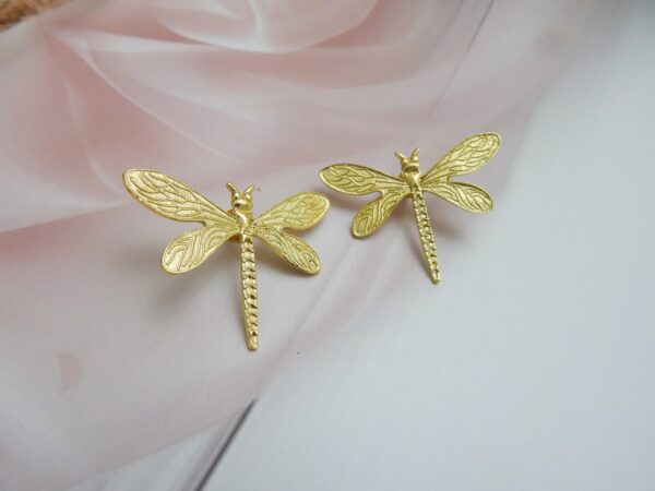 A pair of large, polished gold-tone stud earrings shaped like a dragonfly.