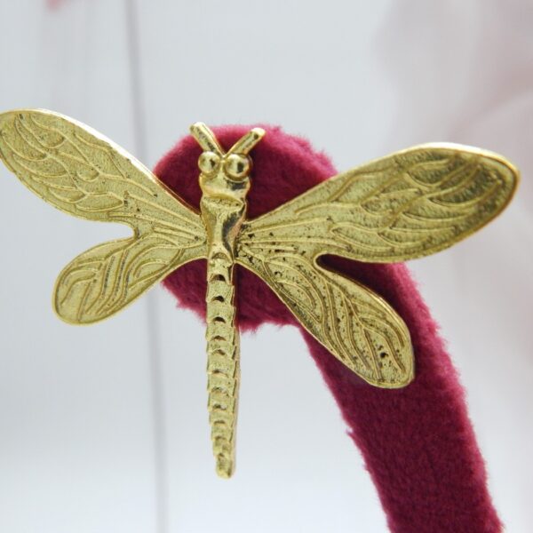 A pair of large, polished gold-tone stud earrings shaped like a dragonfly.