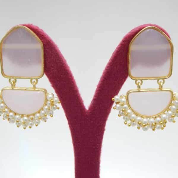 Pearl cluster dangler earrings with blush pink geometric stone and half-moon drop on a display stand