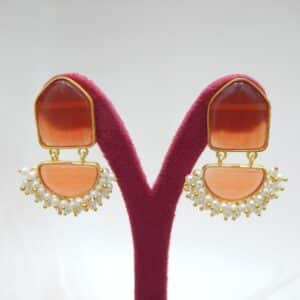Pearl cluster dangler earrings with orange geometric stone and half-moon drop on a display stand