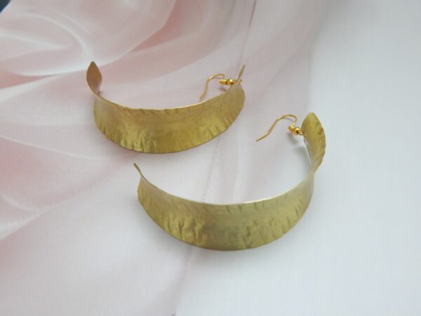 A pair of large, curved, matte gold-tone shield earrings with an artisan hammered texture on fish hooks.
