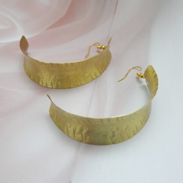 A pair of large, curved, matte gold-tone shield earrings with an artisan hammered texture on fish hooks.