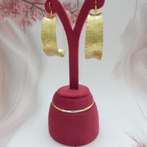 A pair of large, curved, matte gold-tone shield earrings with an artisan hammered texture on fish hooks.