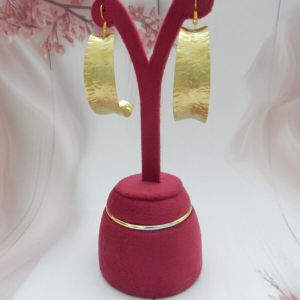 A pair of large, curved, matte gold-tone shield earrings with an artisan hammered texture on fish hooks.