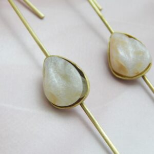 A pair of gold-tone long drop earrings with a natural-looking milky white/peach teardrop stone set on a thin bar.