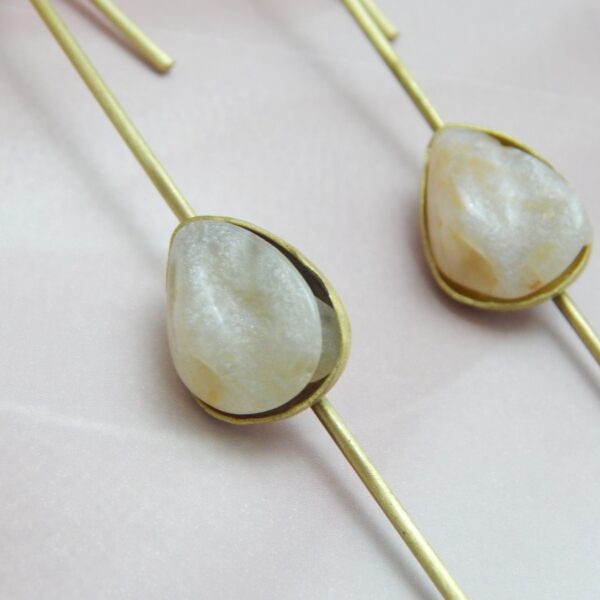 A pair of gold-tone long drop earrings with a natural-looking milky white/peach teardrop stone set on a thin bar.