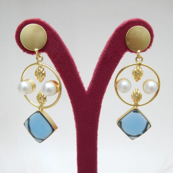 A pair of gold-tone geometric dangle earrings with a circle frame, white pearls, and a large square-shaped blue stone.