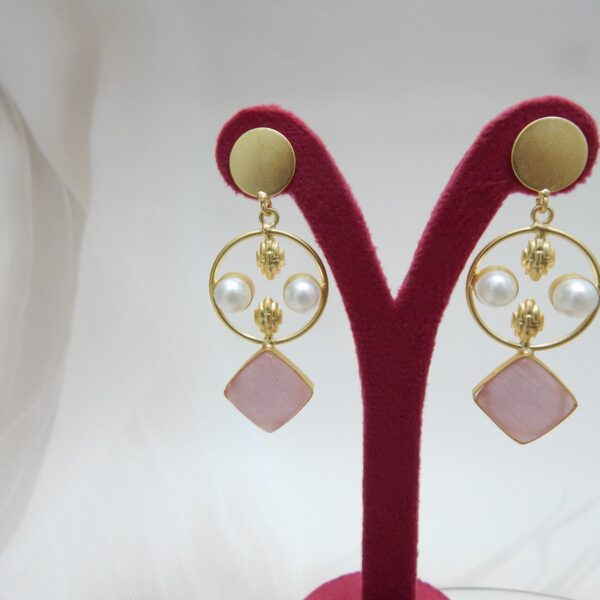 A pair of gold-tone geometric dangle earrings with a circle frame, white pearls, and a large square-shaped blush pink stone.