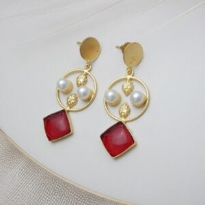 A pair of gold-tone geometric dangle earrings with a circle frame, white pearls, and a large square-shaped red stone.
