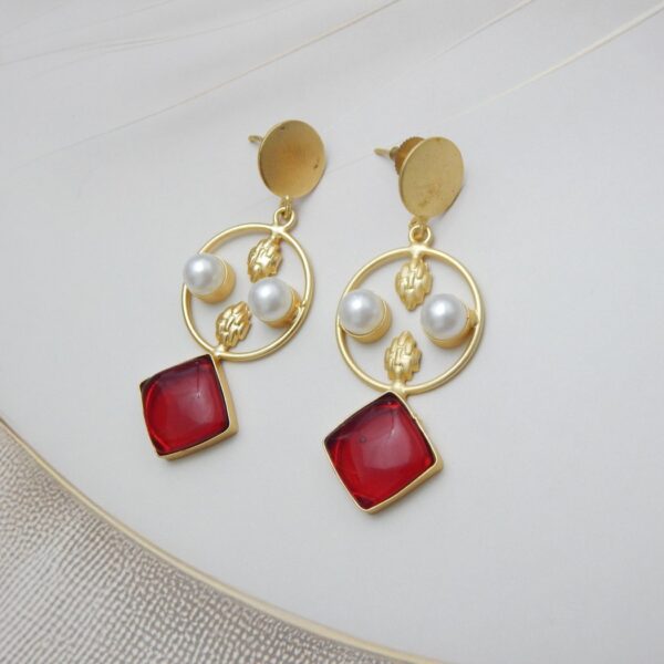 A pair of gold-tone geometric dangle earrings with a circle frame, white pearls, and a large square-shaped red stone.