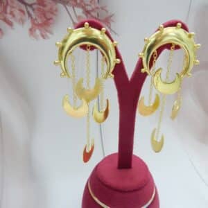 Gold statement crescent moon dangler earrings with chain drops of moon charms displayed on a stand