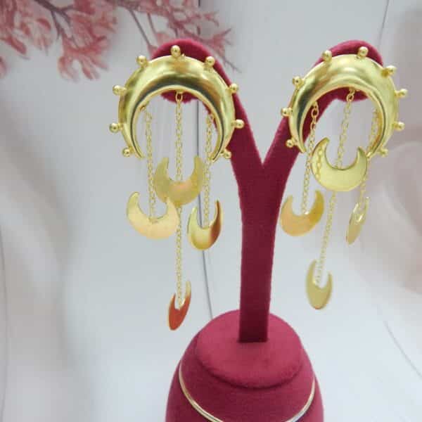 Gold statement crescent moon dangler earrings with chain drops of moon charms displayed on a stand