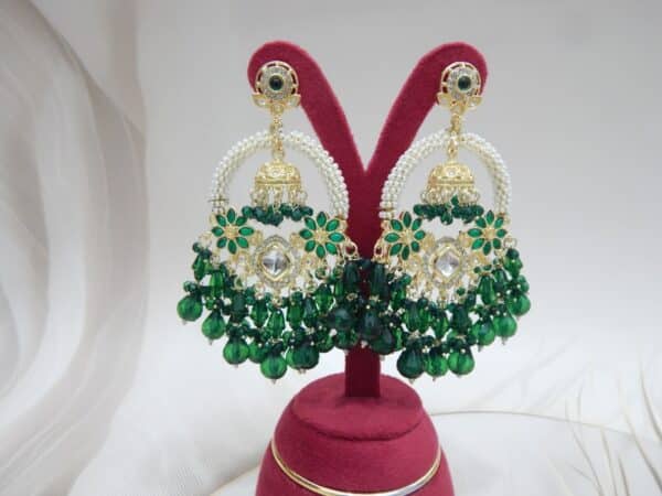 A pair of gold Kundan jhumka earrings with a half-moon design and dark green beaded drops