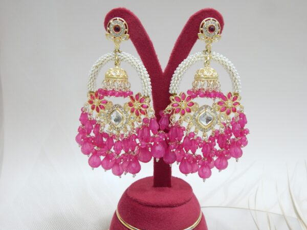 A pair of gold Kundan jhumka earrings with a half-moon design and dangling ruby pink beaded drops