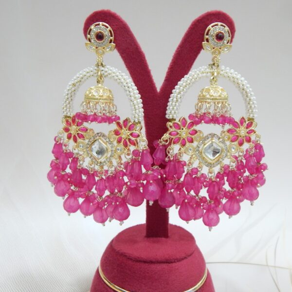 A pair of gold Kundan jhumka earrings with a half-moon design and dangling ruby pink beaded drops