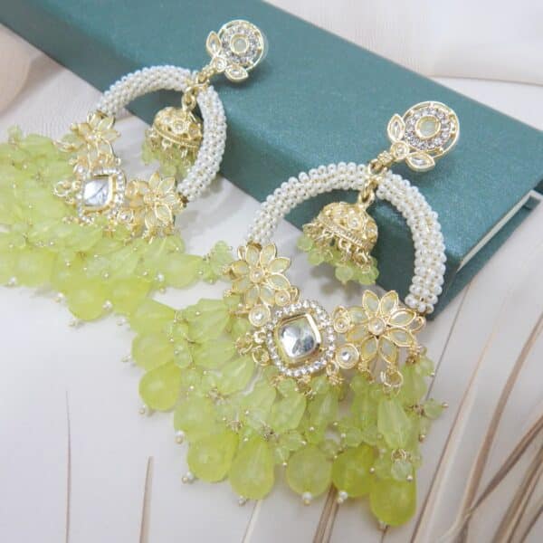 A pair of gold Kundan jhumka earrings with a half-moon design and light green beaded drops
