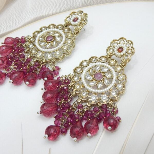 Navratri Purple Jewellery - Royal Reflection DS A pair of large, traditional dangle earrings with a central oval stone, intricate work, a halo of small pearls, and a fan of dangling dark pink colored beads.