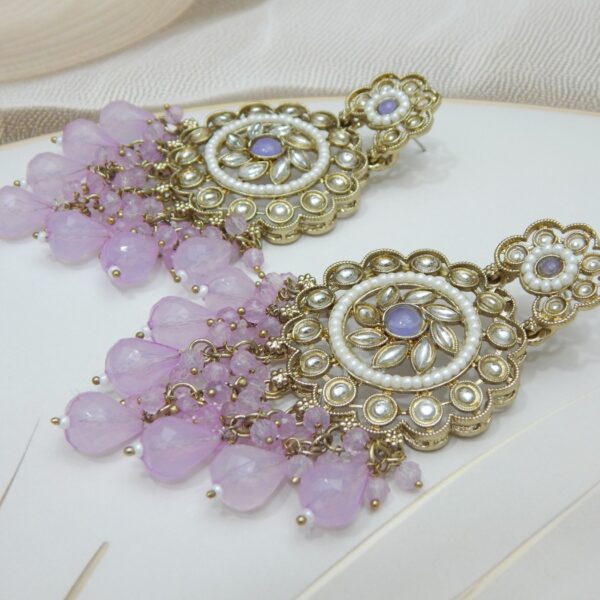 A pair of large, traditional dangle earrings with a central oval stone, intricate work, a halo of small pearls, and a fan of dangling lavender colored beads.