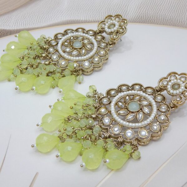 A pair of large, traditional dangle earrings with a central oval stone, intricate work, a halo of small pearls, and a fan of dangling light greencolored beads.