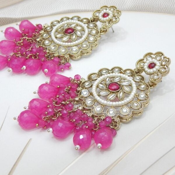 Navratri Purple Jewellery - Royal Reflection DS A pair of large, traditional dangle earrings with a central oval stone, intricate work, a halo of small pearls, and a fan of dangling pink colored beads.